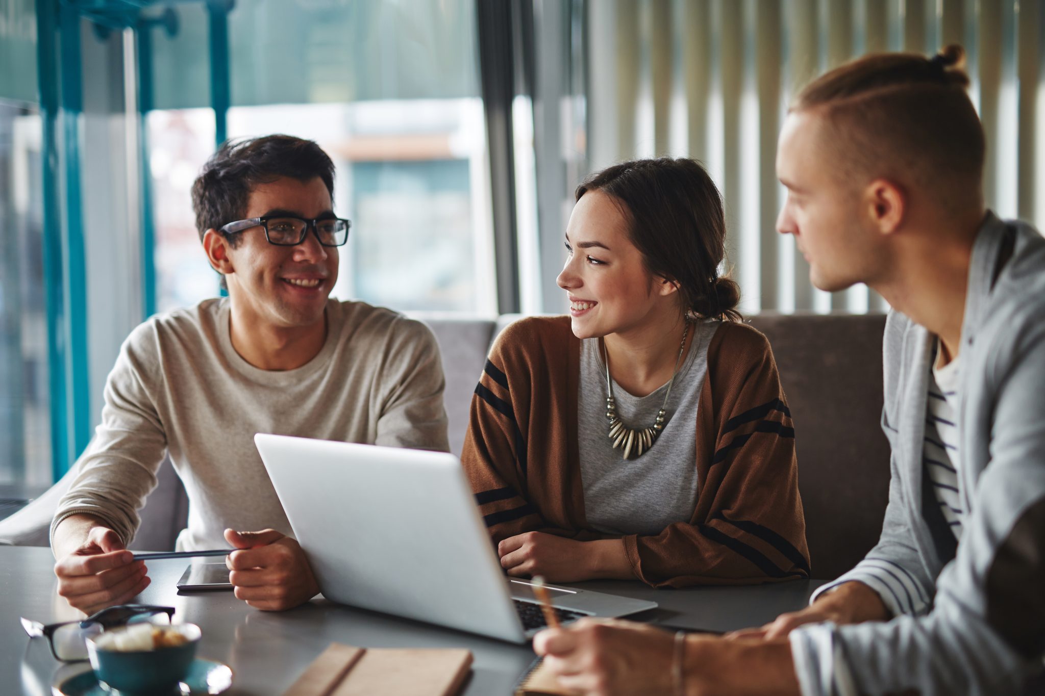 3 smiling individuals look at each other with a computer in front of them
